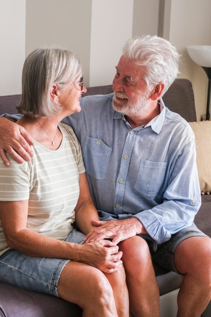 Elderly couple sitting together on a cozy couch at home, smiling and enjoying