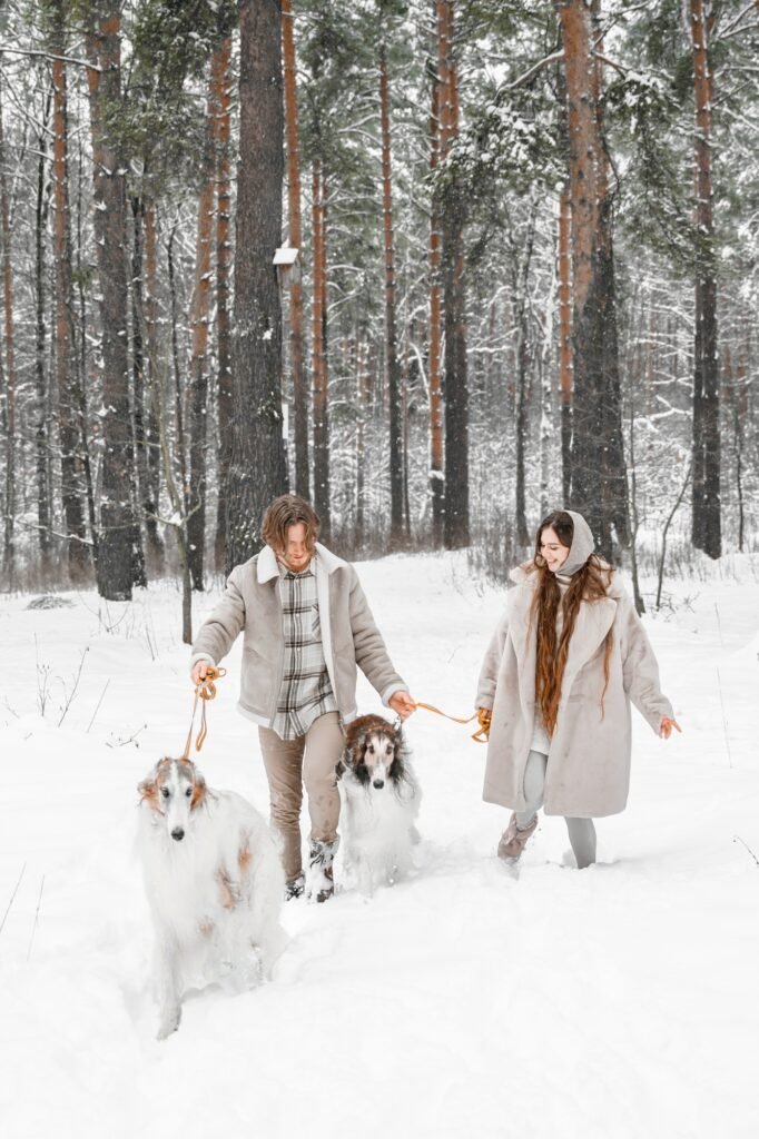 Love romantic young couple girl, guy in snowy cold winter forest walking with pet, dog of hunting